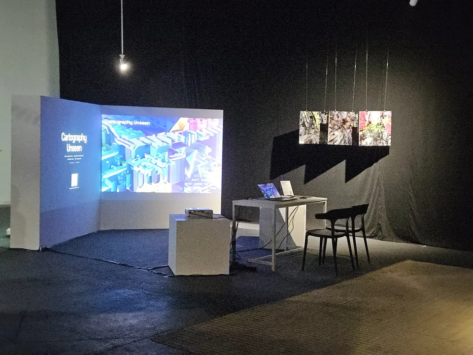 Cartography Unseen installation with a projected game landscape, a play station and suspended prints.